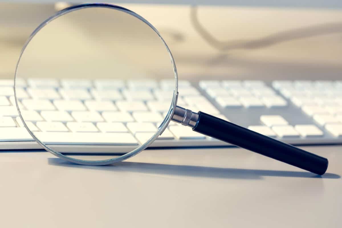 Magnifying glass over white keyboard, symbolizing digital marketing analysis for Make It Loud Digital Marketing.