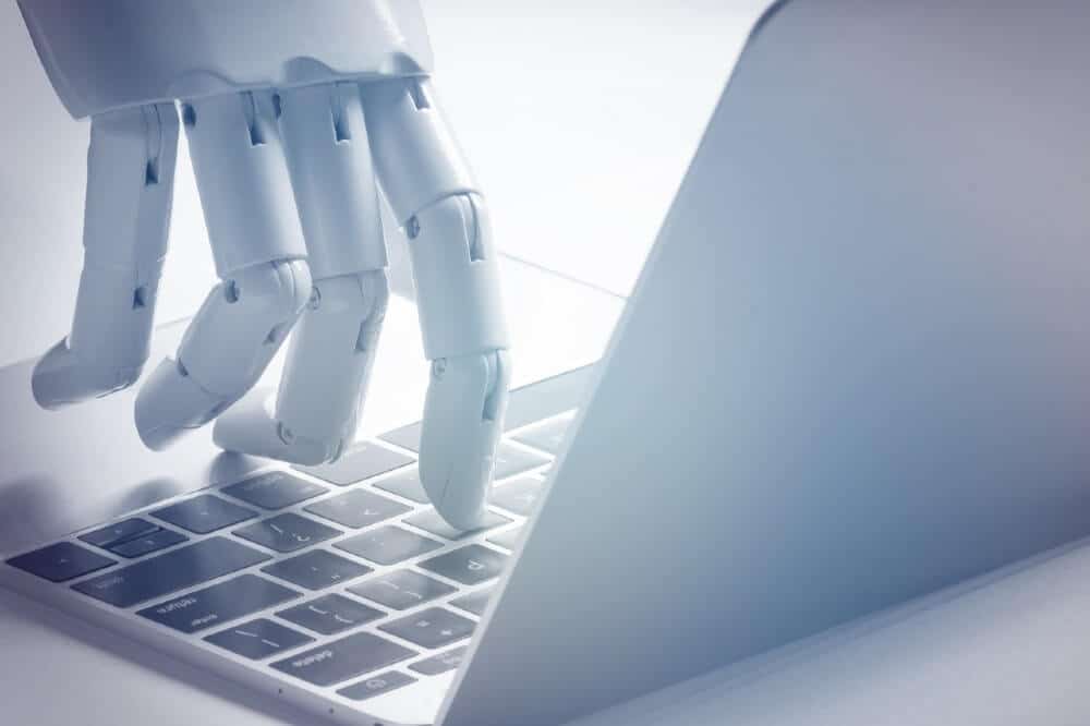 White robot hand typing on silver laptop keyboard, showcasing AI in digital marketing technology and automation solutions.