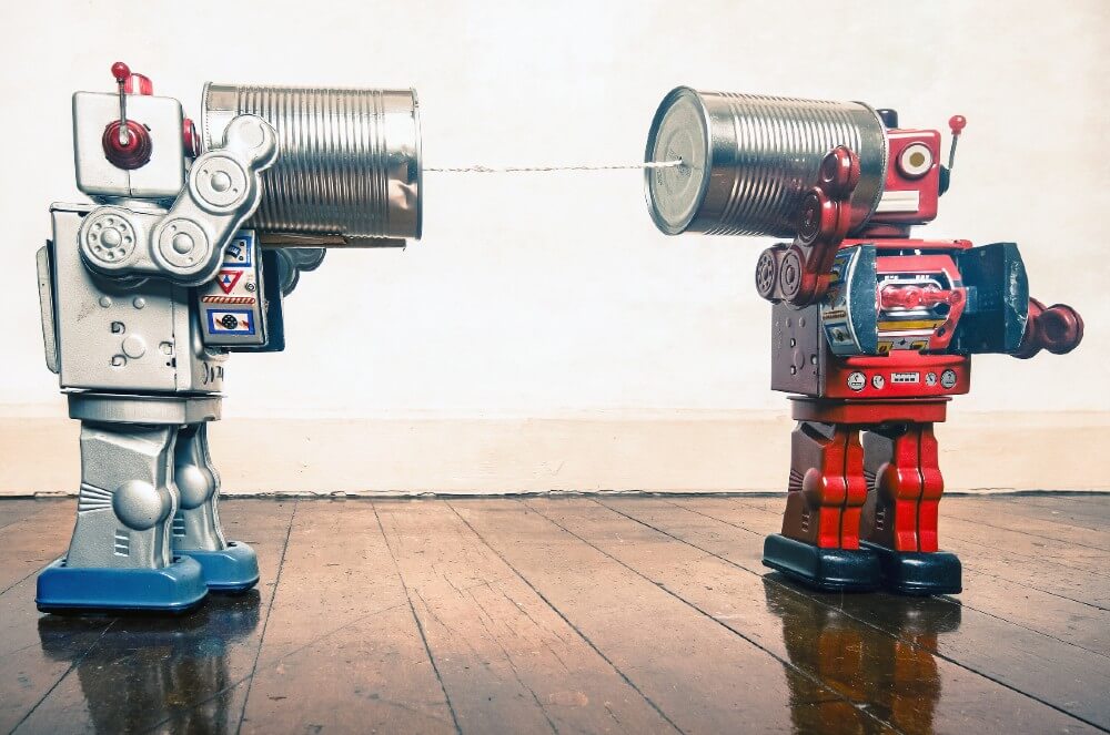 Two retro tin toy robots communicate using tin can telephones on a wooden floor, symbolizing creative digital marketing strategies.