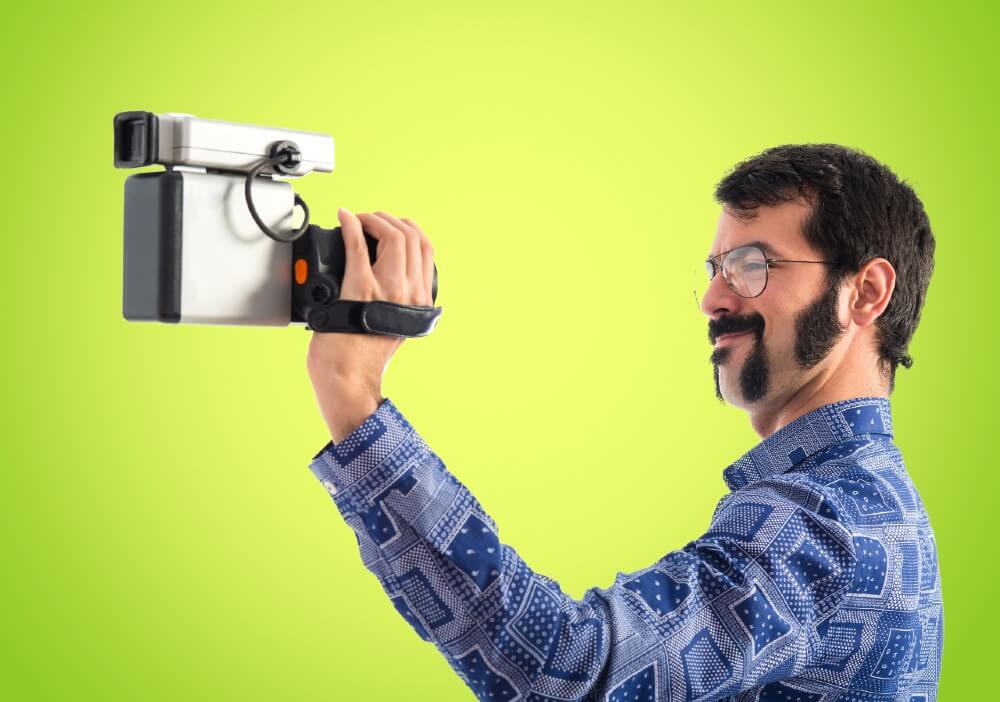 Man in blue patterned shirt filming with handheld video camera against lime green background, digital marketing production setup.