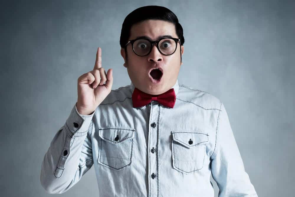 Man wearing a light denim shirt and red bow tie pointing upwards on a gray background, symbolizing digital marketing ideas.