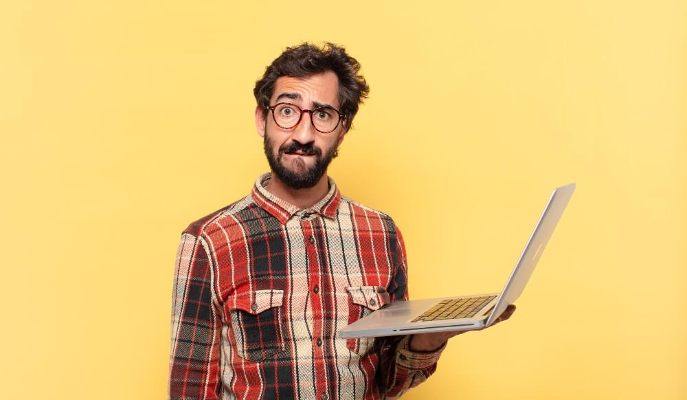 Man in red plaid shirt holding an open laptop in front of a bright yellow background symbolizing digital marketing tools.