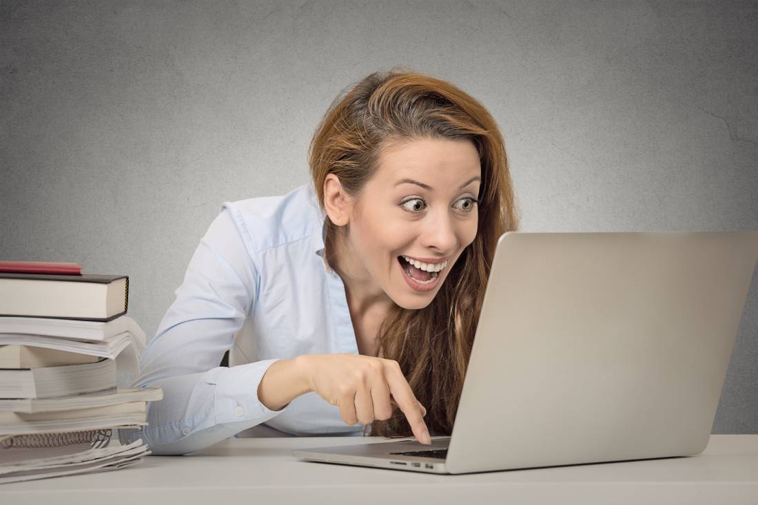 Woman working on laptop pointing at screen, surrounded by books, digital marketing concept for Make It Loud Digital Marketing.